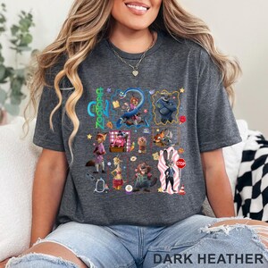May include: Dark heather gray t-shirt featuring a colorful graphic of characters from the animated movie Zootopia. The word "Zootopia" is printed in green and blue. The text "DARK HEATHER" is printed at the bottom of the shirt.