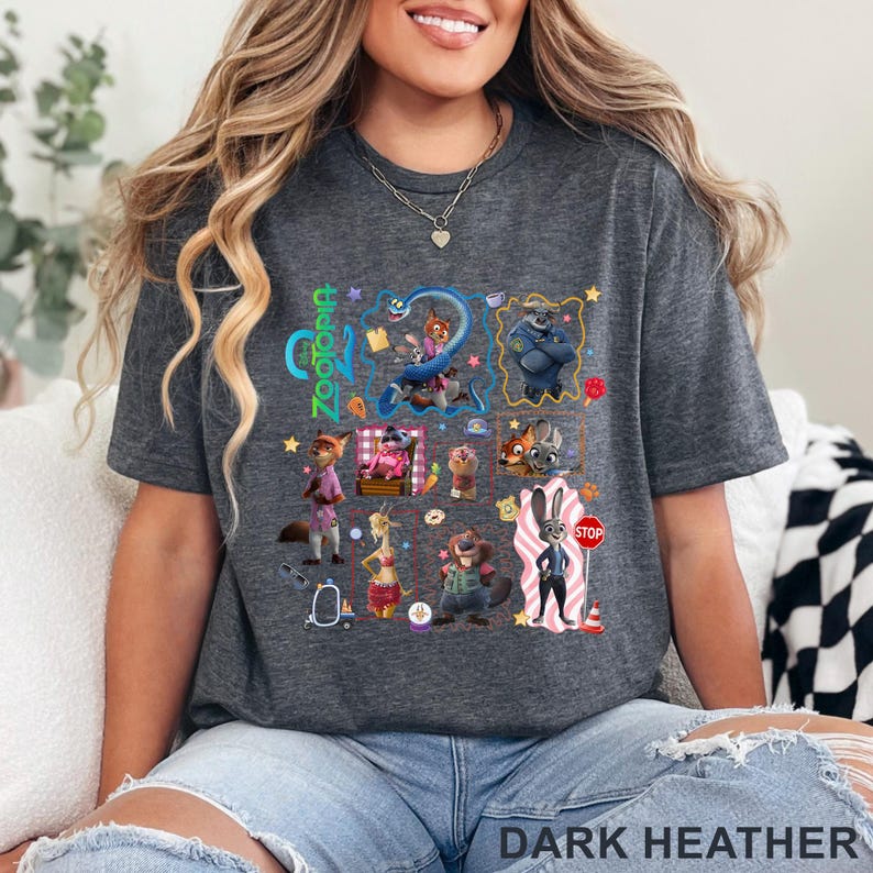 May include: Dark heather gray t-shirt featuring a colorful graphic of characters from the animated movie Zootopia. The word "Zootopia" is printed in green and blue. The text "DARK HEATHER" is printed at the bottom of the shirt.