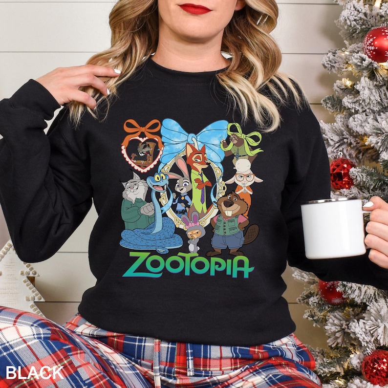 May include: Black sweatshirt featuring a colorful graphic of characters from the animated movie Zootopia. The design includes Judy Hopps, Nick Wilde, and other characters, with the word "Zootopia" in green and blue. The sweatshirt is a crew neck style.