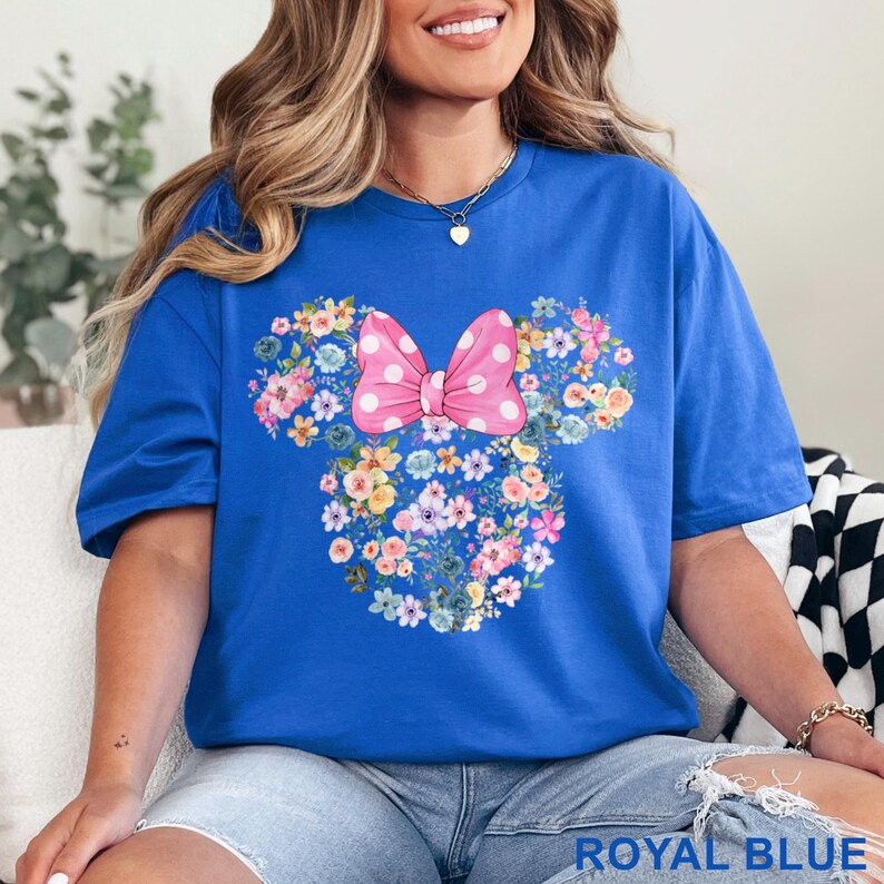 May include: Royal blue t-shirt featuring a floral Minnie Mouse design with a pink polka dot bow. The design is made of various colorful flowers. The text "ROYAL BLUE" is at the bottom of the shirt.