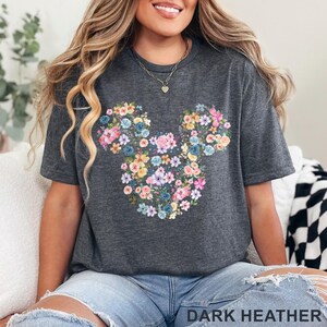 May include: Dark heather gray t-shirt featuring a floral Mickey Mouse design. The design is made up of colorful flowers in shades of pink, blue, yellow, and purple. The text "DARK HEATHER" is at the bottom of the image.