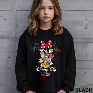 May include: Black sweatshirt featuring a colorful graphic of Disney characters, including Mickey and Minnie Mouse, Donald and Daisy Duck, and Goofy. The design includes a red bow with white polka dots and the words "Disney Trip".