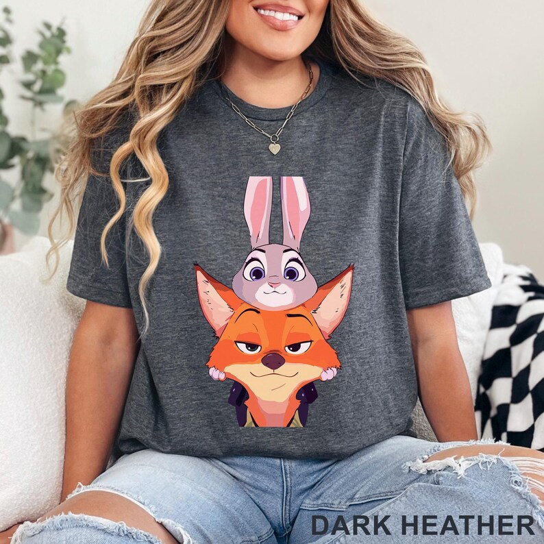 May include: Dark heather gray t-shirt featuring a cartoon image of a fox and a bunny. The fox is orange and the bunny is gray. The text "DARK HEATHER" is printed at the bottom of the shirt.