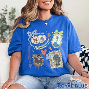 Puede incluir: Camiseta azul real con ilustraciones de personajes de Zootopia en marcos y formas de coraz&oacute;n. El dise&ntilde;o incluye a Nick Wilde, Judy Hopps y otros personajes. La palabra "Zootopia" est&aacute; impresa verticalmente en el lado izquierdo.