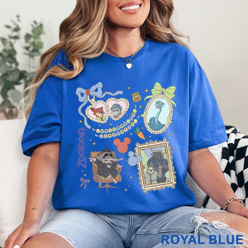 Puede incluir: Camiseta azul real con ilustraciones de personajes de Zootopia en marcos y formas de coraz&oacute;n. El dise&ntilde;o incluye a Nick Wilde, Judy Hopps y otros personajes. La palabra "Zootopia" est&aacute; impresa verticalmente en el lado izquierdo.