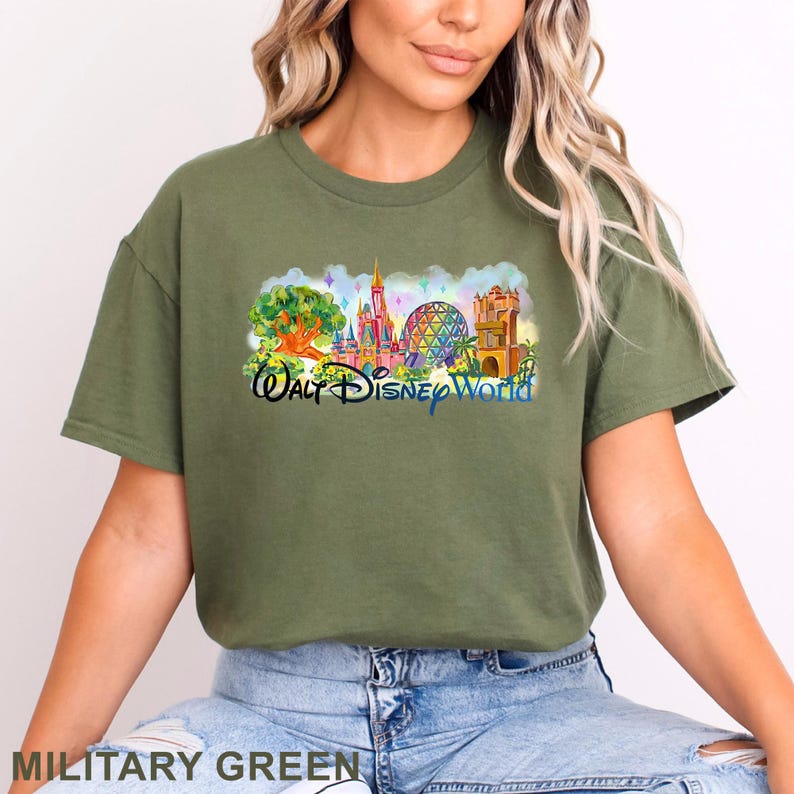 May include: An olive green t-shirt featuring a colorful graphic print of the Walt Disney World skyline, including the Tree of Life, Cinderella Castle, Spaceship Earth, and the Tower of Terror, with the text Walt Disney World printed in blue.