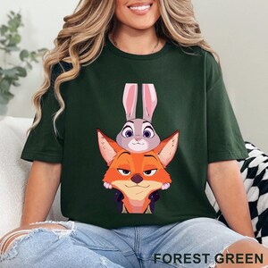 May include: Forest green t-shirt featuring a cartoon image of Judy Hopps the bunny and Nick Wilde the fox. The characters are stacked on top of each other. The text "FOREST GREEN" is at the bottom of the image.