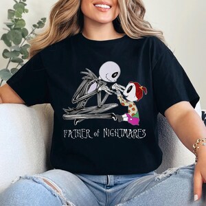 Puede incluir: Camiseta negra con un gr&aacute;fico de Jack Skellington y un ni&ntilde;o. El dise&ntilde;o los muestra interactuando. El texto "FATHER OF NIGHTMARES" est&aacute; impreso en blanco debajo.