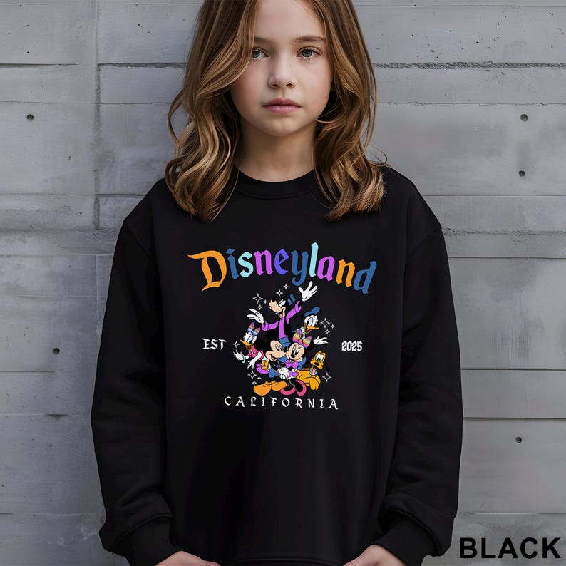 Puede incluir: Sudadera negra con el logotipo de Disneyland en degradado de colores. El dise&ntilde;o incluye personajes de dibujos animados y el texto "EST 2025 CALIFORNIA". La sudadera es de cuello redondo.