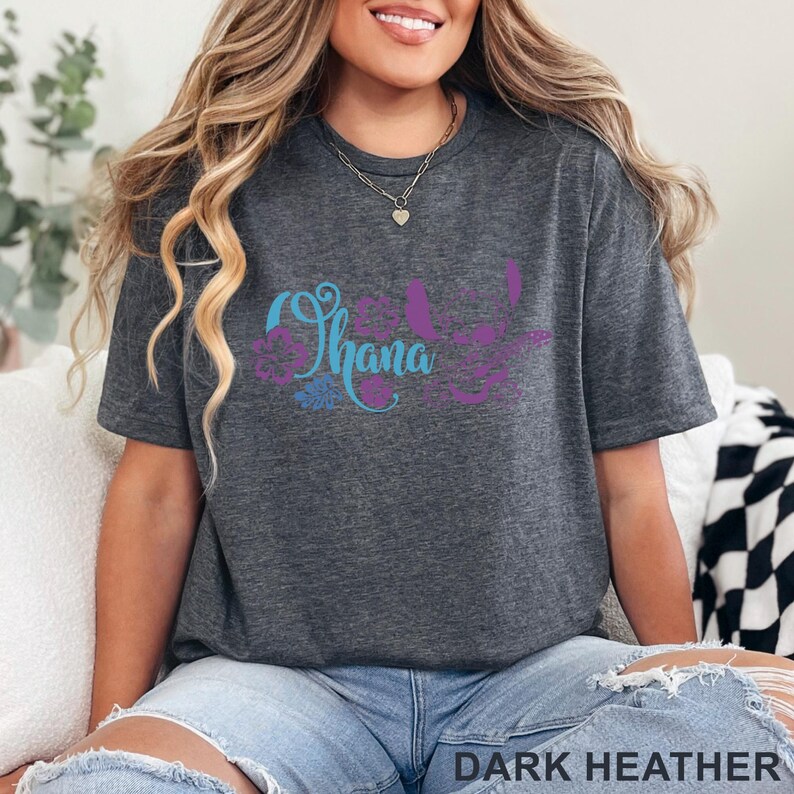Op de afbeelding: Een donkergrijs gem&ecirc;leerd T-shirt met korte mouwen en een grafische print in blauw en paars. Het ontwerp bevat het woord Ohana in cursief schrift, omringd door bloemaccenten en een gestileerd silhouet van een karakterfiguur.
