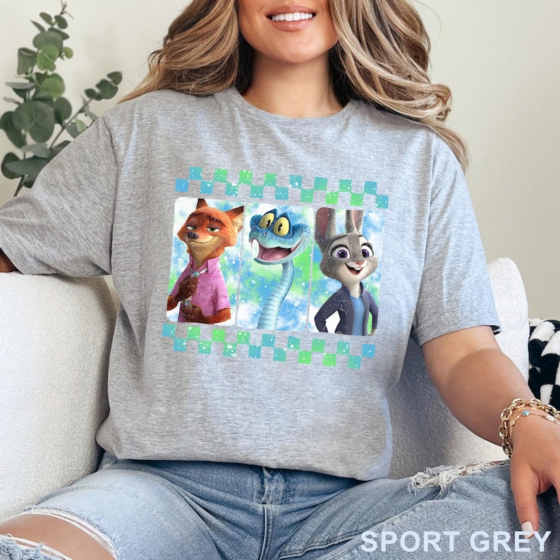 May include: Sport grey t-shirt featuring three cartoon characters: a fox in a pink shirt, a blue snake, and a rabbit in a blue jacket. The design is framed with a blue and green checkered pattern. The words "SPORT GREY" are printed at the bottom.