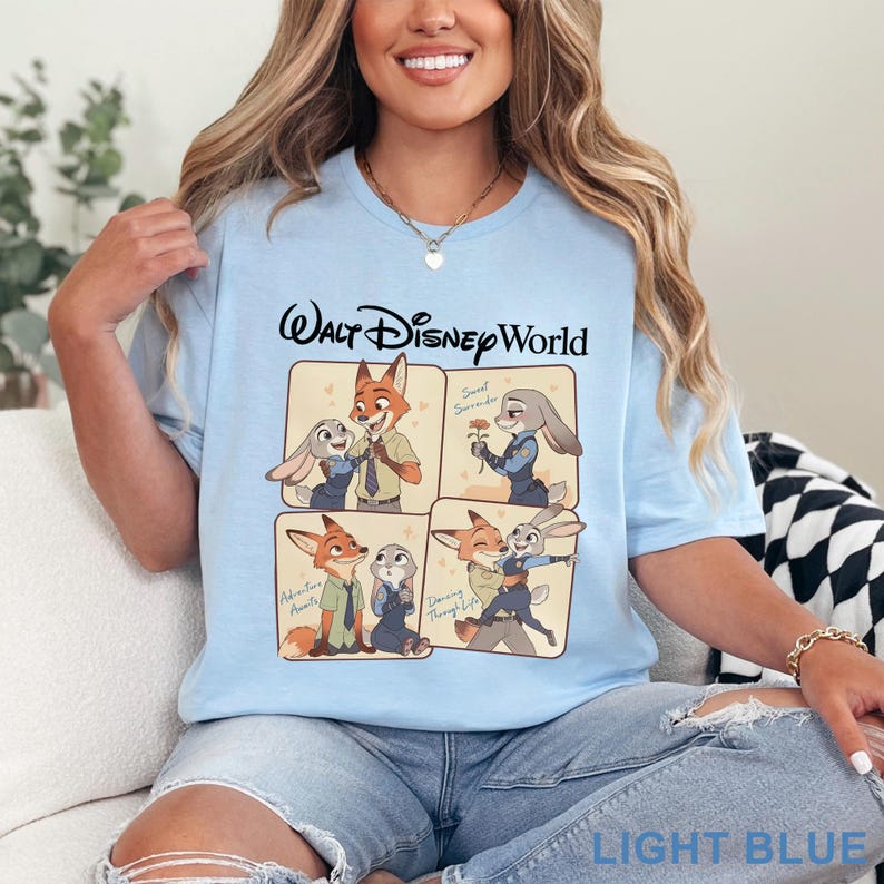May include: Light blue t-shirt featuring a graphic of Nick Wilde and Judy Hopps from Zootopia, with the text "Walt Disney World." The graphic includes four panels with different scenes of the characters. The shirt is labeled "Light Blue."