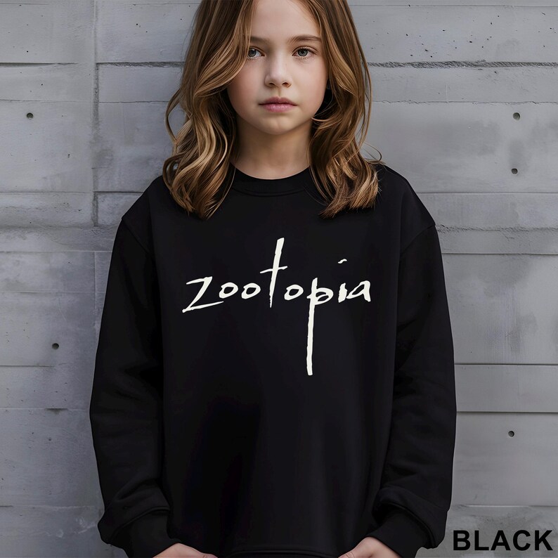May include: Black sweatshirt with the word "Zootopia" in white script. The sweatshirt is worn by a person with long, wavy brown hair. The word "BLACK" is printed in a sans-serif font at the bottom right corner.