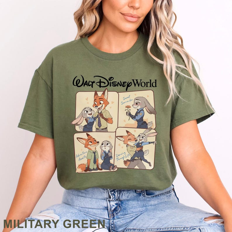 May include: Military green t-shirt featuring a four-panel illustration of Zootopia characters. The top reads "Walt Disney World" in black script. The panels show Nick Wilde and Judy Hopps in various poses. The shirt is made of a soft material.