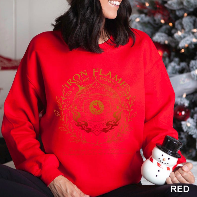 May include: A red sweatshirt with a gold graphic design featuring the text "IRON FLAME BURN IT DOWN" in a circular pattern. The design includes floral elements and a central emblem. The word "RED" is in the bottom right corner.