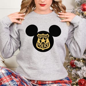May include: A light gray sweatshirt featuring a black Mickey Mouse silhouette with a gold and black police badge design. The badge reads "Zootopia Police" with a star in the center. The text "Sport Grey" is at the bottom.