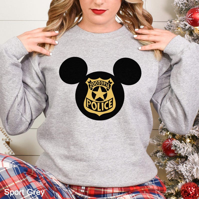 May include: A light gray sweatshirt featuring a black Mickey Mouse silhouette with a gold and black police badge design. The badge reads "Zootopia Police" with a star in the center. The text "Sport Grey" is at the bottom.