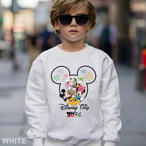 May include: White sweatshirt featuring a Mickey Mouse head design with colorful fireworks and Disney characters. The text "Disney Trip 2020" is printed below the graphic. The sweatshirt is a solid white color.