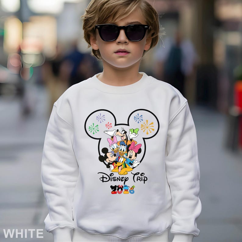 May include: White sweatshirt featuring a Mickey Mouse head design with colorful fireworks and Disney characters. The text "Disney Trip 2020" is printed below the graphic. The sweatshirt is a solid white color.