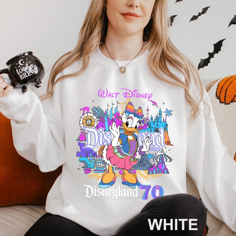 May include: White sweatshirt featuring a colorful graphic of Daisy Duck in front of Disneyland landmarks. The design includes the text "Walt Disney Disneyland 70". The sweatshirt is a comfortable, casual style.