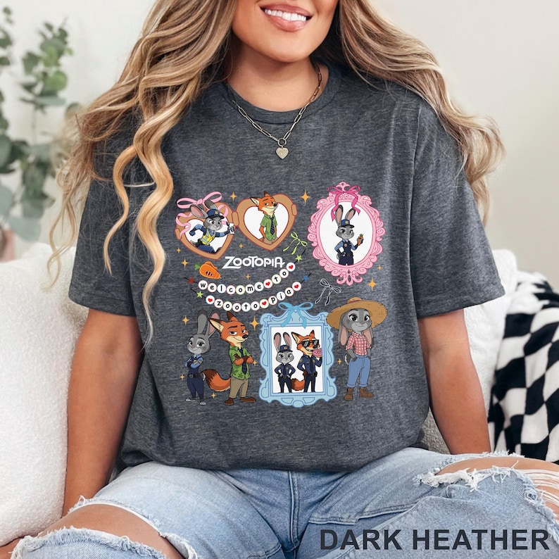May include: Dark heather gray t-shirt featuring a colorful graphic of characters from the animated movie Zootopia. The design includes framed portraits of a fox and a rabbit, with the word "Zootopia" in the center. The shirt is made of a soft material.