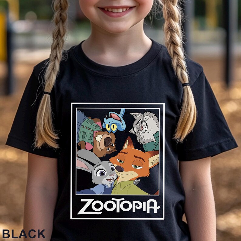May include: Black t-shirt with a graphic of characters from the animated film Zootopia. The design features Judy Hopps, Nick Wilde, and other characters within a white frame. The word "ZOOTOPIA" is printed in white below the characters.