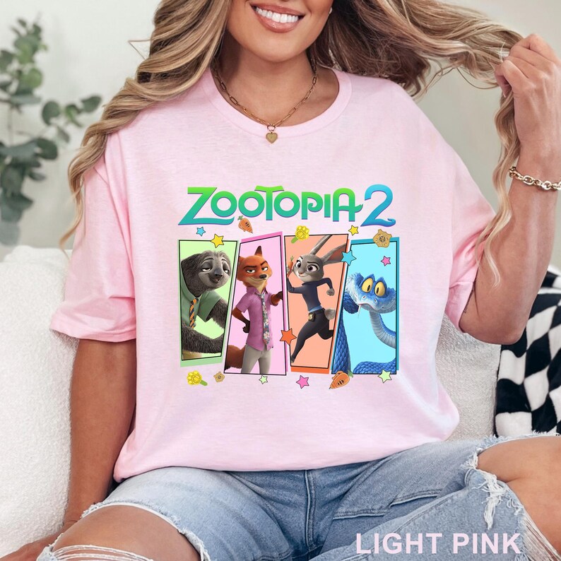 May include: Pale pink t-shirt with the text "ZOOTOPIA 2" in green and a graphic of characters from the movie. The graphic includes a sloth, fox, rabbit, and snake. The words "LIGHT PINK" are printed at the bottom.