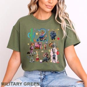 May include: Military green t-shirt featuring a colorful graphic of characters from the animated movie Zootopia. The design includes various animal characters and the movie's title. The shirt is a comfortable, casual style.