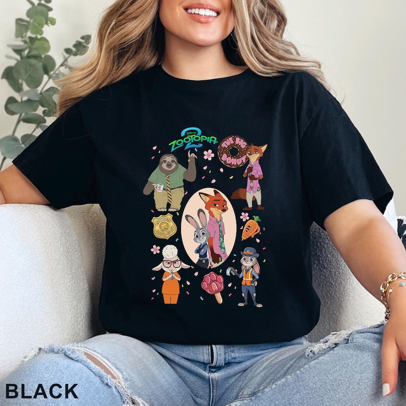 May include: Black t-shirt featuring a colorful graphic of characters from the animated movie Zootopia. The design includes the movie title, a sloth, a fox, a bunny, and other characters. The word "BLACK" is printed at the bottom.