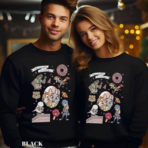 May include: Black sweatshirts featuring a colorful cartoon design with characters, a donut, and text. The design includes a bear, fox, rabbit, and other elements. The text reads "The Big Donut" and "You gotta do it."
