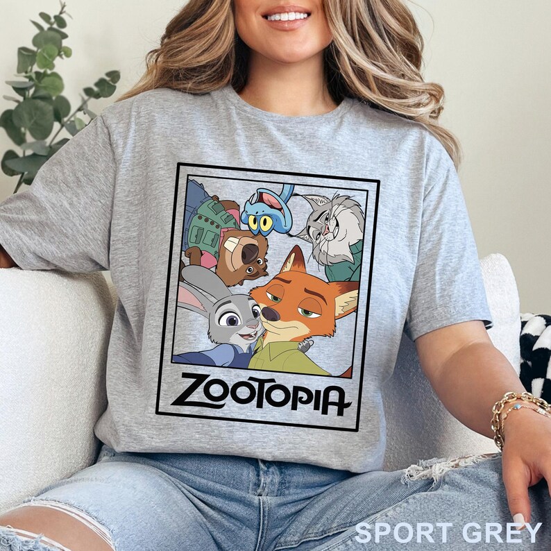May include: Light grey sport t-shirt with a "Zootopia" graphic. The design features characters from the animated film, including Judy Hopps and Nick Wilde, within a framed image, with the movie title below. The shirt is a light grey colour.
