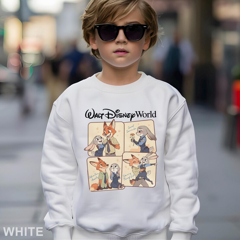 May include: White sweatshirt featuring the text "Walt Disney World" in black script. The sweatshirt has a four-panel graphic of Zootopia characters. The word "WHITE" is printed at the bottom of the sweatshirt.