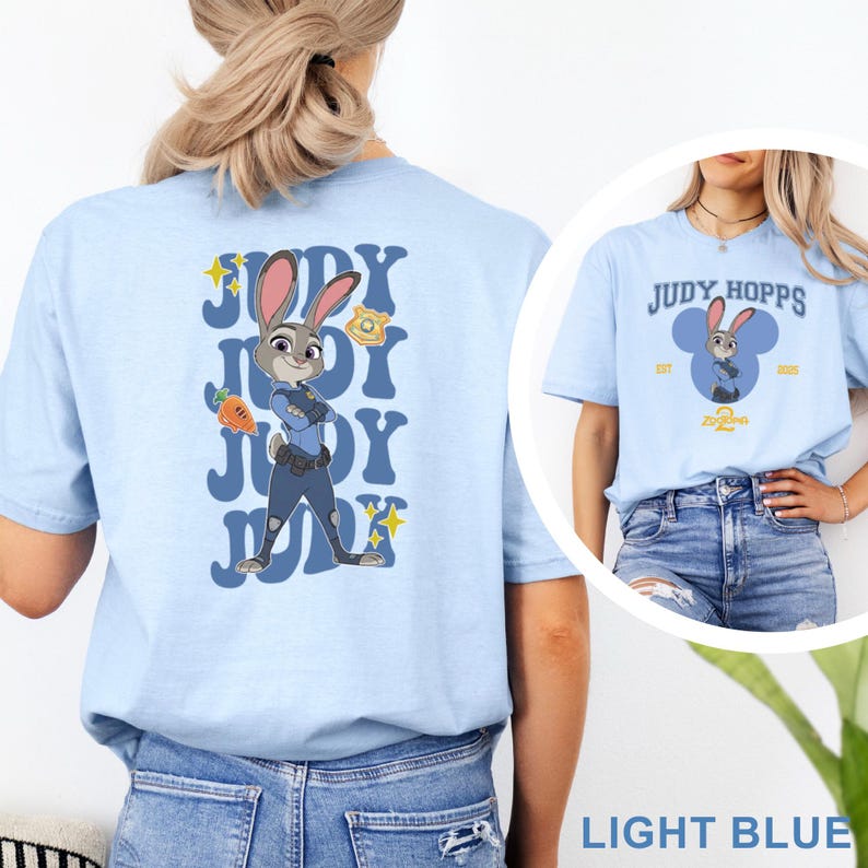 May include: Light blue t-shirt featuring Judy Hopps from Zootopia. The back of the shirt displays a graphic of Judy in her police uniform with the text "JUDY" repeated. The front of the shirt has a Judy Hopps design with the text "JUDY HOPPS".