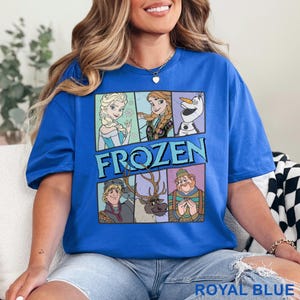 May include: Royal blue t-shirt featuring a graphic of characters from the movie "Frozen." The design includes Elsa, Anna, Olaf, Kristoff, Sven, and a man. The word "FROZEN" is displayed in large, blue letters. The shirt is a solid royal blue color.