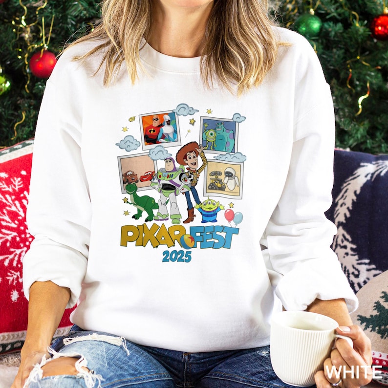 Może przedstawiać: Biała bluza z kolorową grafiką postaci z film&oacute;w Pixar i napisem "PIXAR FEST 2025". Projekt zawiera obrazy Woody'ego, Buzza Astrala i innych postaci z film&oacute;w Pixar. Bluza jest w stylu casual.