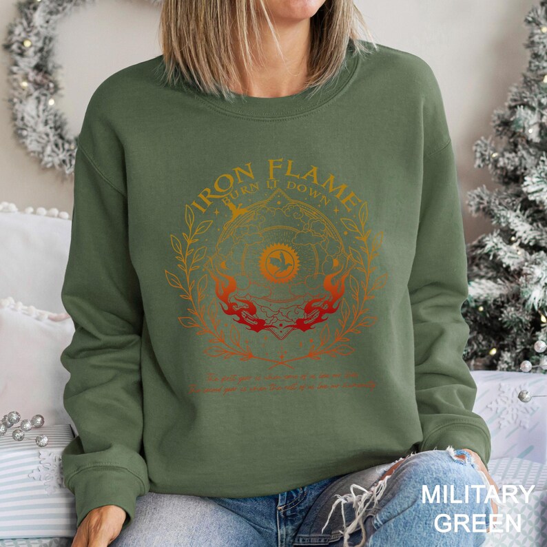 May include: Military green sweatshirt with the text "IRON FLAME BURN IT DOWN" in orange and red. The design features a circular emblem with flames and floral elements. The sweatshirt is a crew neck style.
