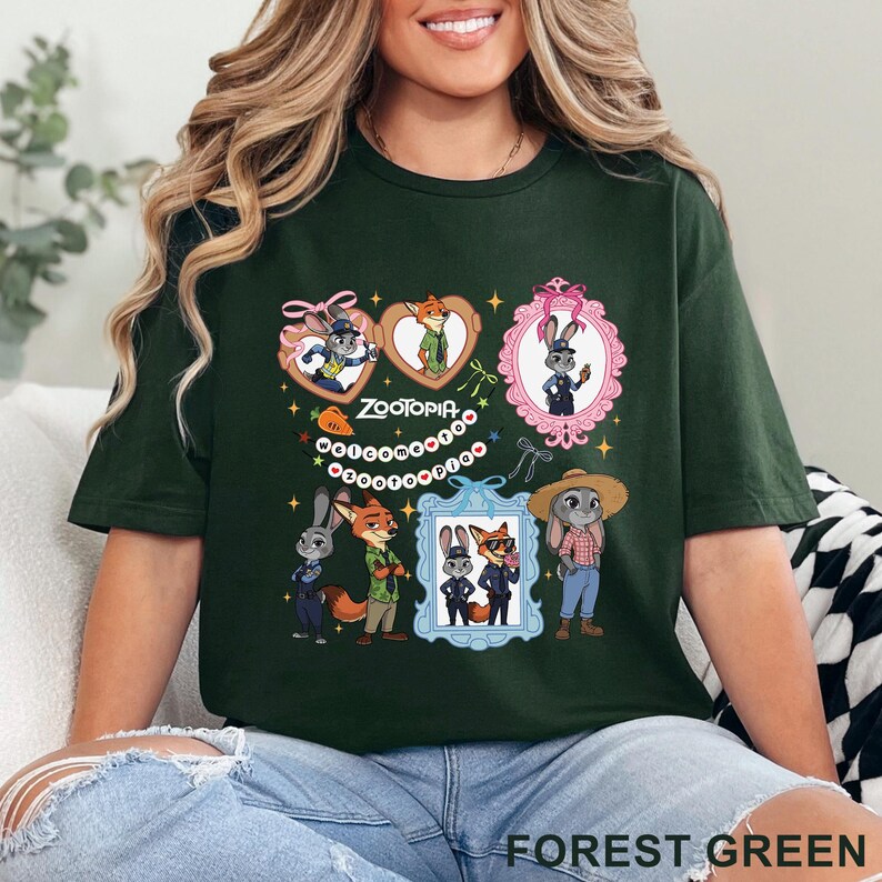 Puede incluir: Una camiseta verde bosque con un estampado gr&aacute;fico de los personajes de Zootopia, incluyendo a Judy Hopps y Nick Wilde. El dise&ntilde;o incluye varias ilustraciones enmarcadas, peque&ntilde;as estrellas, lazos y el texto "Welcome to Zootopia" en c&iacute;rculo.