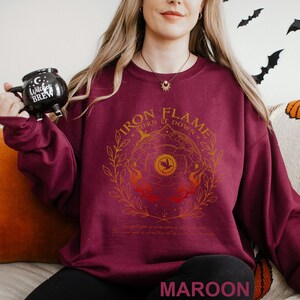 May include: Maroon sweatshirt with a gold and orange graphic that reads "Iron Flame Turn it Down". The design includes a circular emblem with a bird and flames. The text "MAROON" is at the bottom.