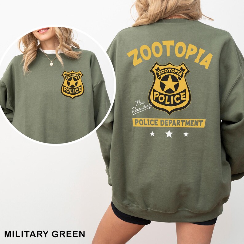 May include: Military green sweatshirt featuring the text "ZOOTOPIA" and a police badge graphic on the back and front. The badge has a star in the center and the word "POLICE". The sweatshirt also has the text "POLICE DEPARTMENT" and "Now Recruiting".