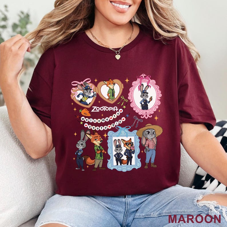 Puede incluir: Una camiseta de manga corta color granate con un estampado gr&aacute;fico de Zootopia. El dise&ntilde;o incluye varias ilustraciones de Judy Hopps y Nick Wilde en marcos, junto con el texto "ZOOTOPIA" y "welcome to zootopia" rodeado de peque&ntilde;as estrellas.