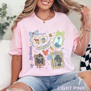 Puede incluir: Camiseta rosa claro con un dise&ntilde;o gr&aacute;fico colorido con personajes y elementos de la pel&iacute;cula animada "Zootopia". El dise&ntilde;o incluye retratos enmarcados, lazos y la palabra "Zootopia" en una fuente estilizada. La camiseta es de material suave.