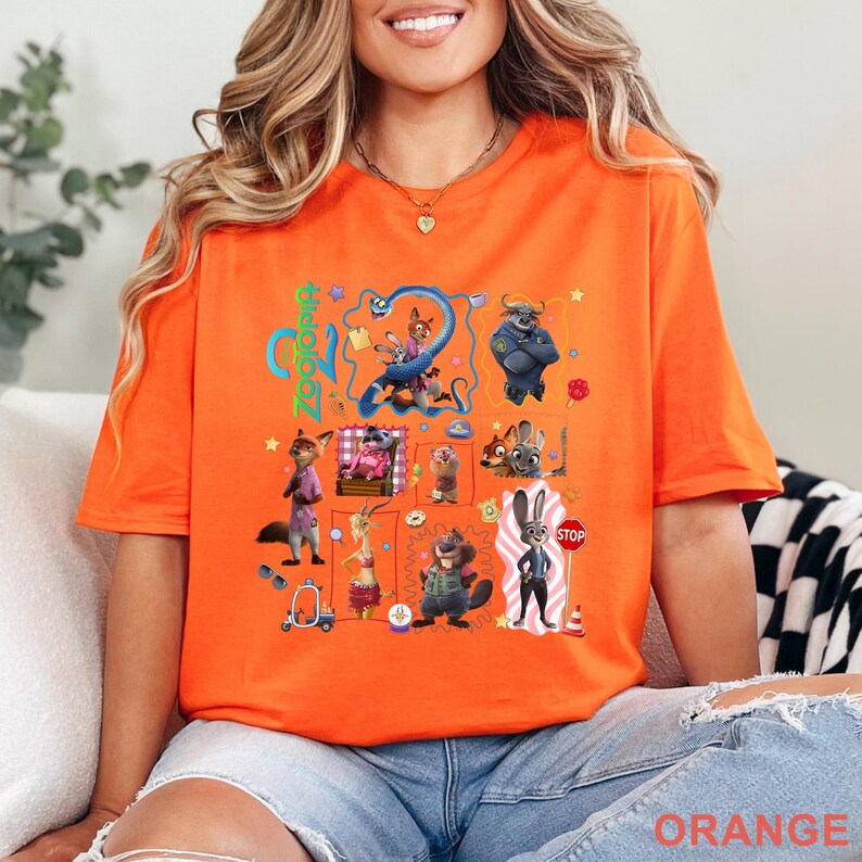 May include: Orange t-shirt featuring a colorful graphic design with characters and the word "Zootopia". The design includes various cartoon animals and the word "STOP". The word "ORANGE" is printed at the bottom.