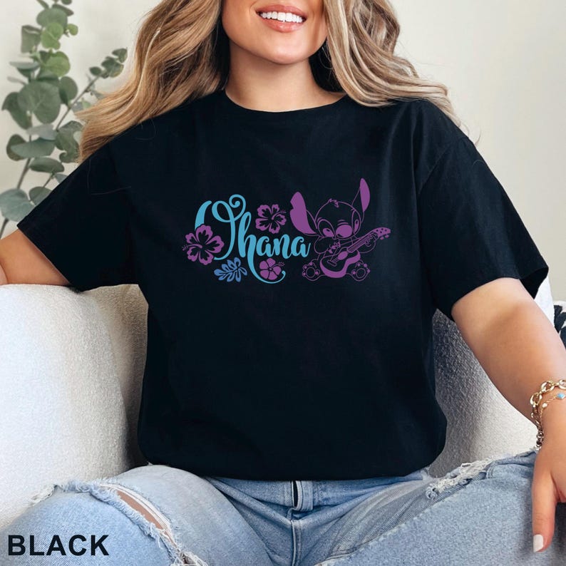 May include: Black t-shirt featuring the word "Ohana" in teal and purple floral design, with a purple cartoon character playing a ukulele. The word "BLACK" is printed at the bottom of the shirt.