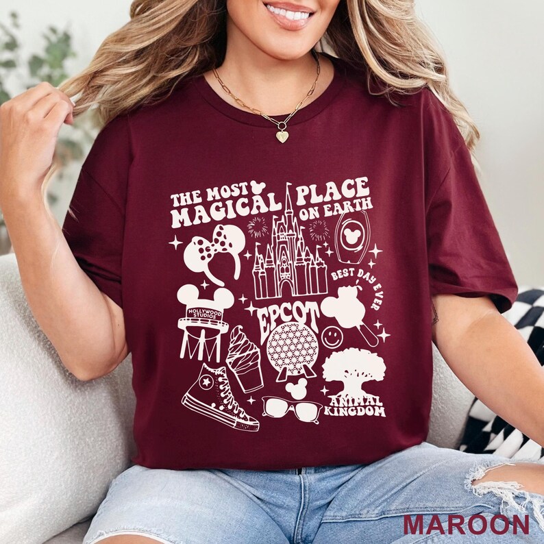 May include: Maroon t-shirt with a white graphic design featuring Disney icons and the text "THE MOST MAGICAL PLACE ON EARTH". The design includes a castle, Mickey Mouse ears, and other park-related images. The word "MAROON" is at the bottom.