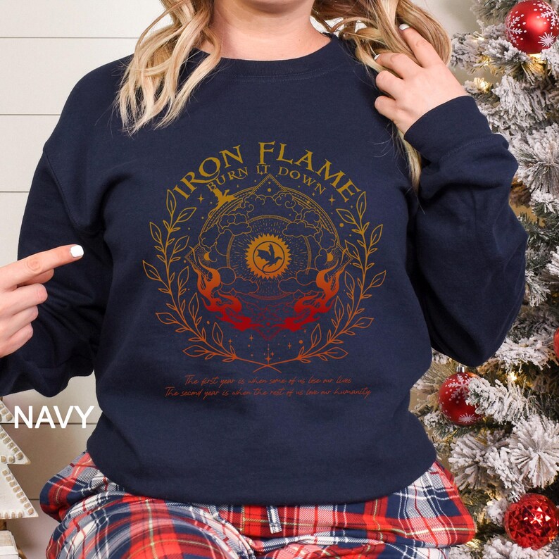 May include: Navy blue sweatshirt with a circular graphic design in gold and red, featuring the text "IRON FLAME TURN IT DOWN". The design includes a bird, flames, and botanical elements. The text "NAVY" is visible on the left side.