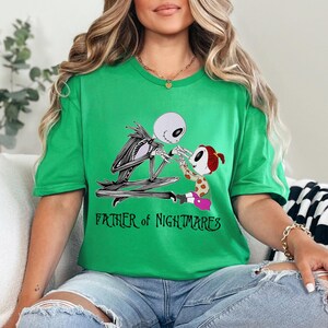 Puede incluir: Camiseta verde con un dise&ntilde;o de Jack Skellington y una figura infantil. El texto "FATHER OF NIGHTMARES" est&aacute; impreso debajo. La camiseta es de material suave. El dise&ntilde;o es de Pesadilla antes de Navidad.