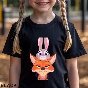 May include: Black t-shirt featuring a cartoon image of Judy Hopps the bunny and Nick Wilde the fox from Zootopia. The word "BLACK" is printed at the bottom of the shirt.