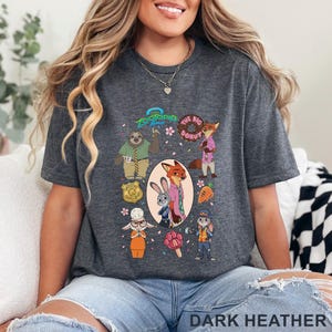 K&ouml;nnte beinhalten: Ein dunkelgrau meliertes T-Shirt mit einem Zootopia-Grafikdruck. Das Design zeigt Charaktere wie Judy Hopps und Nick Wilde, eine Polizeimarke, einen Donut, eine Karotte und ein pfotenf&ouml;rmiges Eis am Stiel, umgeben von kleinen rosa Bl&uuml;tenbl&auml;ttern.
