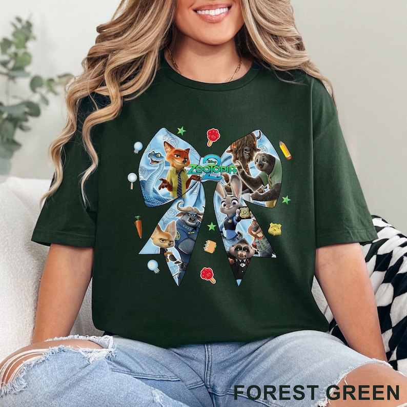 Op de afbeelding: Bosgroen T-shirt met een groot strikdesign met personages uit de animatiefilm "Zootopia". De strik is gevuld met afbeeldingen van de personages en het woord "Zootopia" staat in het midden gedrukt. Het shirt is effen van kleur.