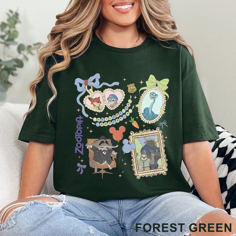 Puede incluir: Camiseta verde bosque con ilustraciones de dibujos animados de personajes de Zootopia. El dise&ntilde;o incluye retratos enmarcados, corazones y lazos. La palabra "Zootopia" est&aacute; impresa verticalmente en el lado izquierdo de la camiseta.